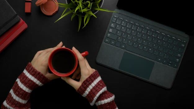 A person is working at a laptop on a dark wooden modern table with a mug and notebook with pen, showcasing the process of uploading and licensing photos to stock agencies. The surrounding environment is minimalist and clean, suggesting a professional home office setup.