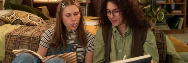 Two roommates studying together in their dorm room, surrounded by textbooks and laptops. They are collaborating on a project and discussing notes.
